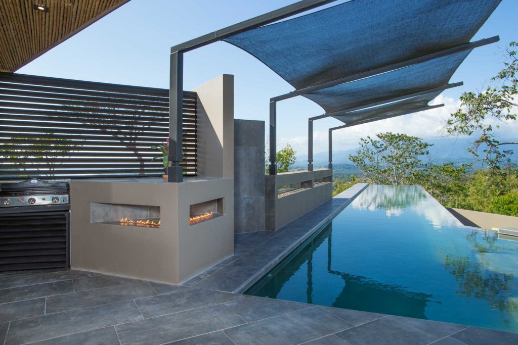 The pool deck has a modern BBQ grill and a unique fire pit that runs along its edge. 
