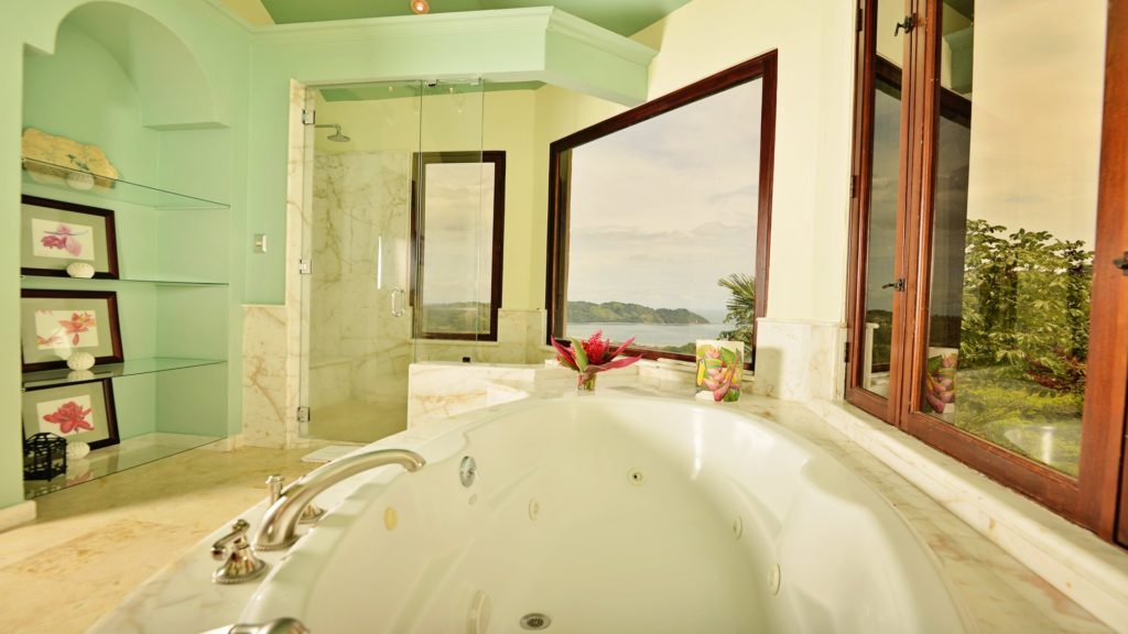 Bathe in extravagance amidst this opulent bathroom oasis, where a lavish bathtub, sleek shower, and panoramic view of the ocean and lush forest converge in perfect harmony.