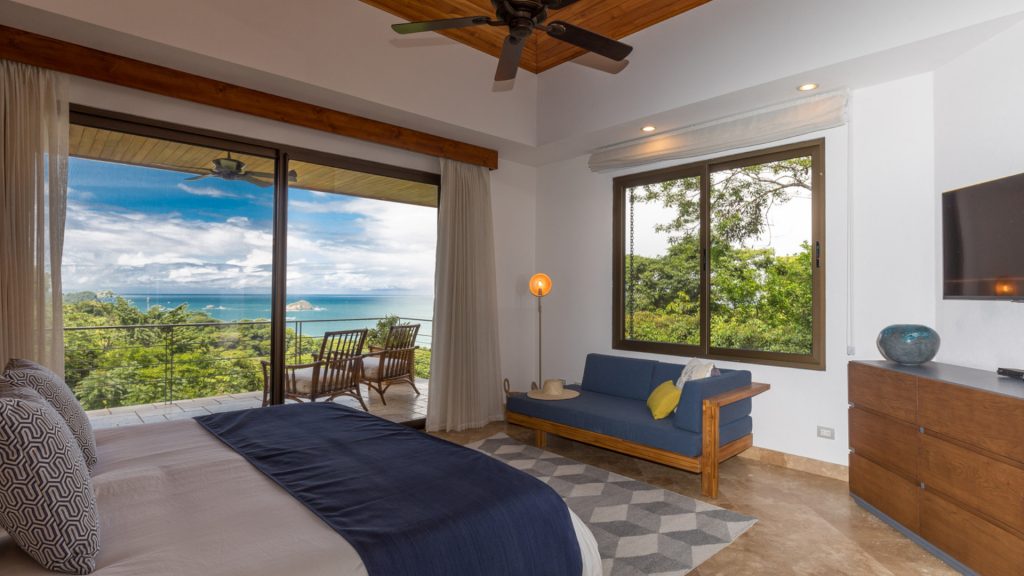 A luxury bedroom with relaxing seating and access to an ocean-view balcony to step out for some ocean breeze.
