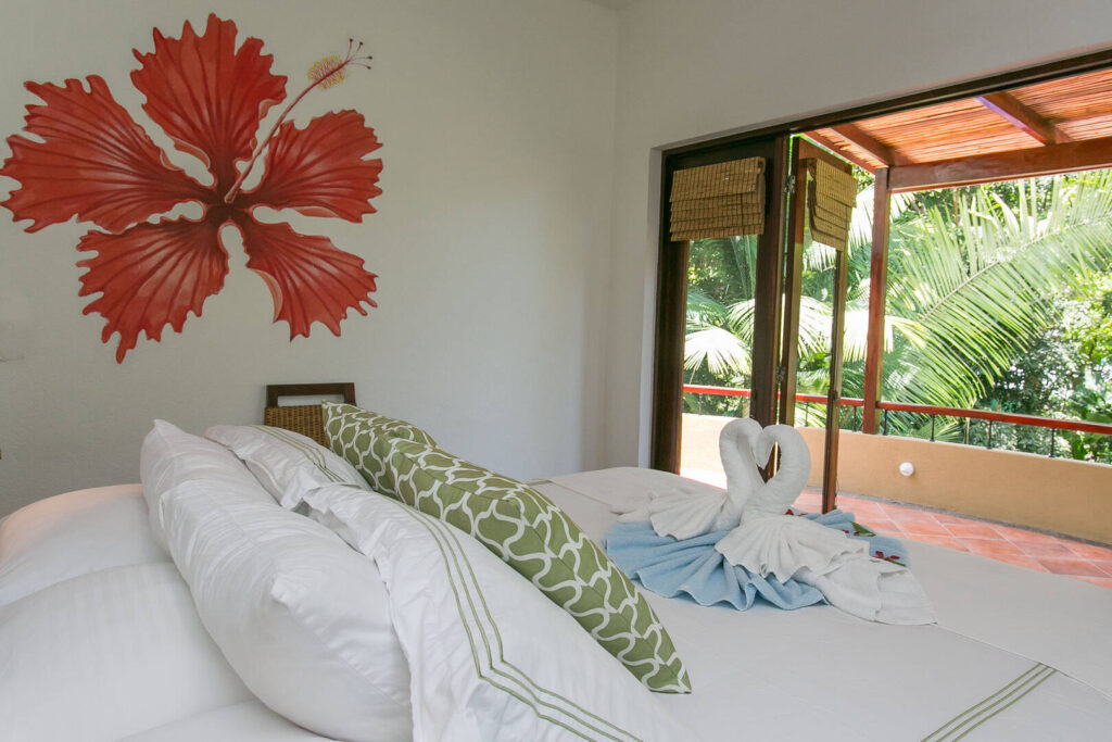 Beautiful wall art and tropical plants surrounding the balcony help to create this relaxing bedroom.