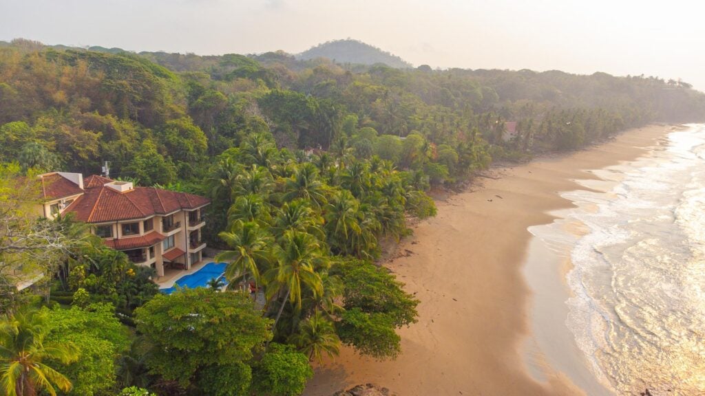 Aerial view of a luxury beachfront vacation villa on Playa Tambor, Costa Rica, surrounded by tropical rainforest.