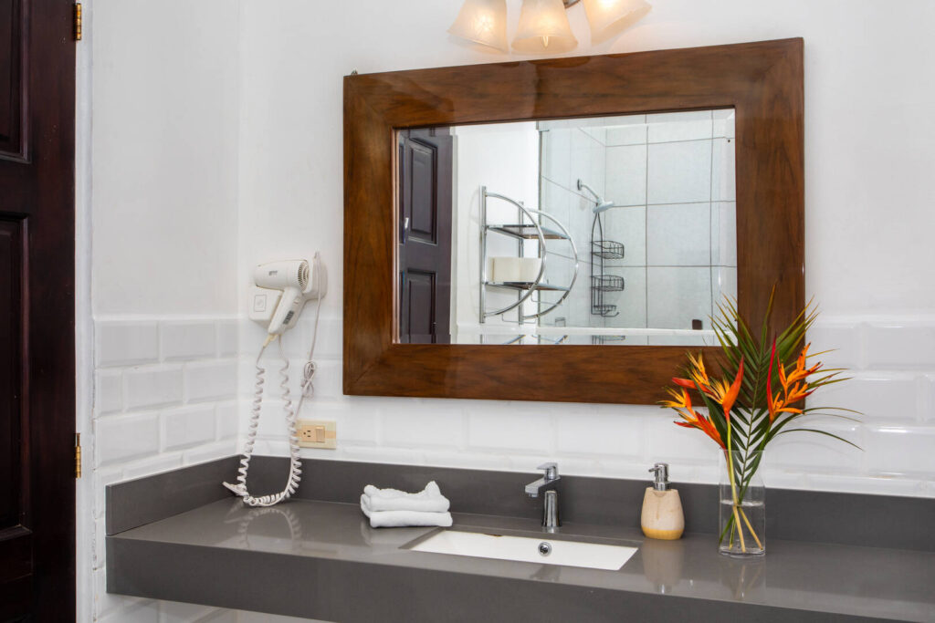 This bathroom has clean white tiles, a stone counter top, and a stunning mirror framed in natural wood.