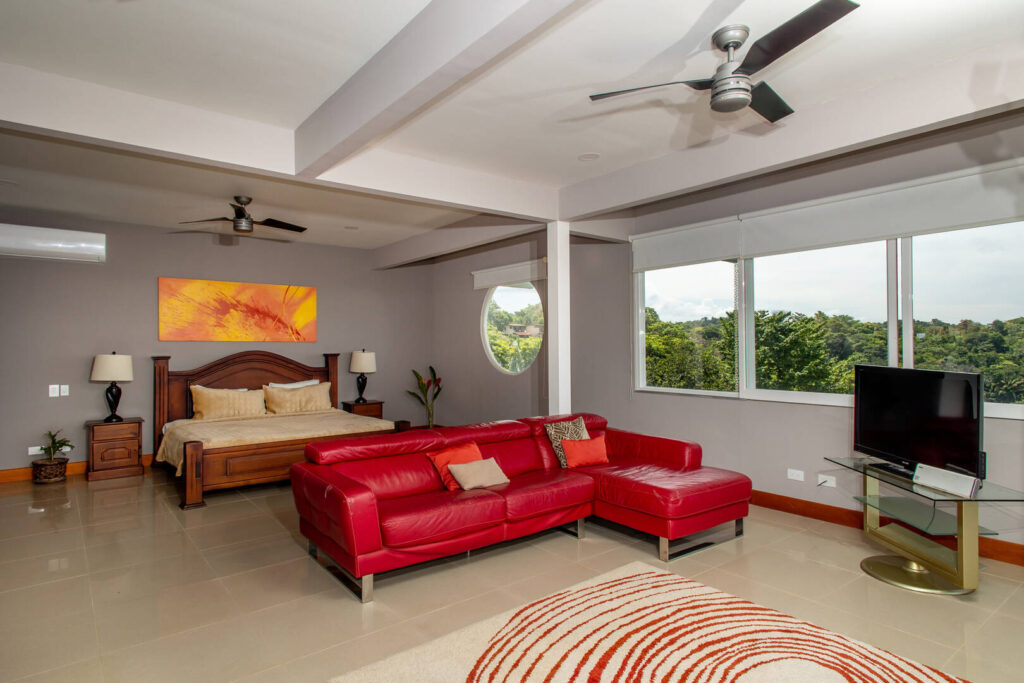 This huge air-conditioned bedroom has a unique circular window and a cool seating area with a large-screen TV.