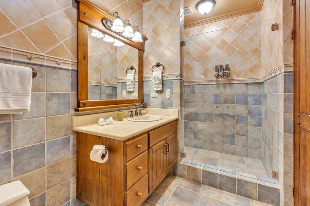 The private ensuite bathroom offers a spacious walk-in rain shower, handcrafted wood vanity, and elegant tropical finishes.