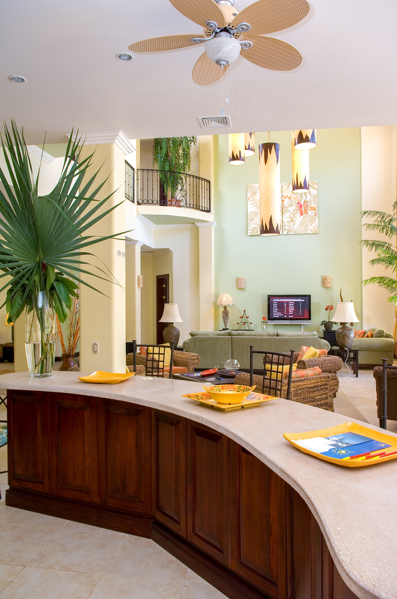 Curved kitchen bar overlooking a high-ceiling great room with wicker seating and pendant lights inside a Los Sueños villa in Jacó Costa Rica.
