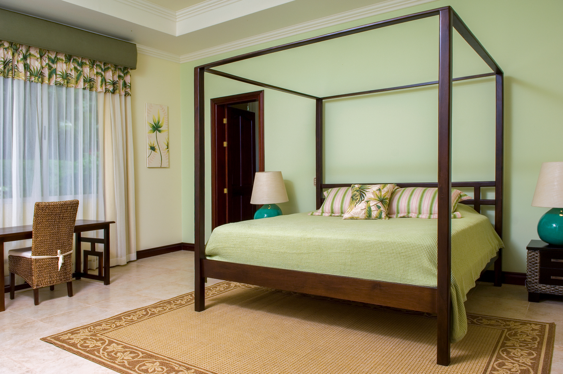 King bedroom with dark wood four-poster canopy bed, bedside lamps, desk, and window with curtains inside a Los Sueños villa in Jacó Costa Rica.