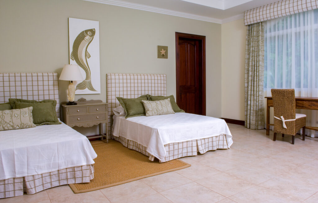 A spacious bedroom with two beds, coastal-inspired décor, and a quiet desk area beside the window.