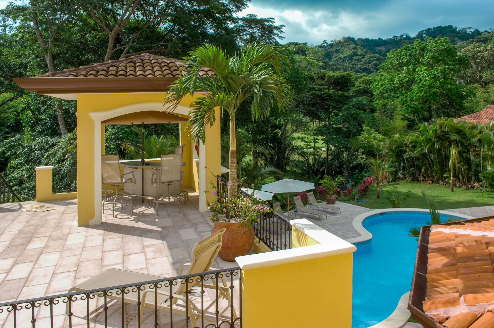 Covered terrace with seating area overlooking private pool and tropical landscaping at a Los Sueños villa.