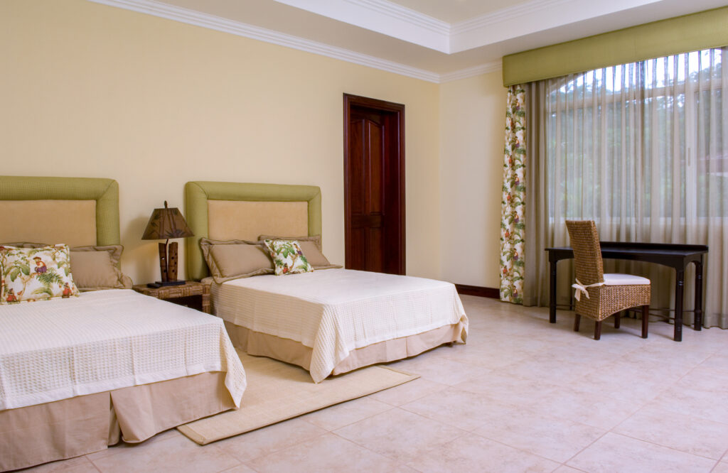 A spacious bedroom with two beds and a quiet desk area beside a large window.
