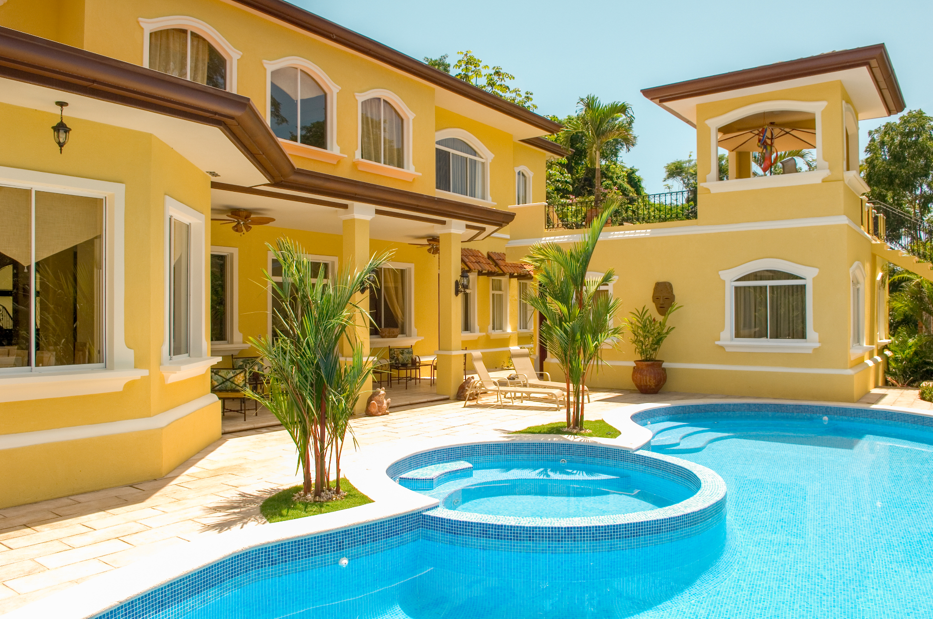 Private swimming pool with round jacuzzi beside a yellow Los Sueños resort villa with covered terrace and tropical landscaping.