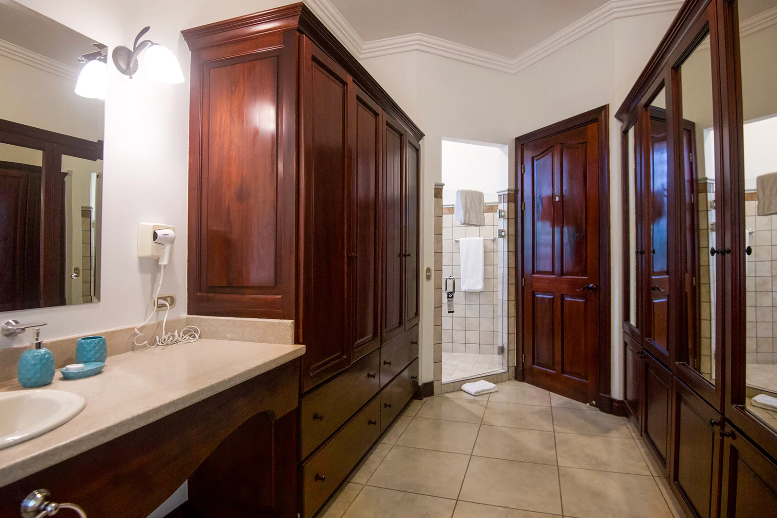 Ensuite bathroom with wood cabinetry, vanity sink, mirrors, and walk-in shower inside a Los Sueños villa.
