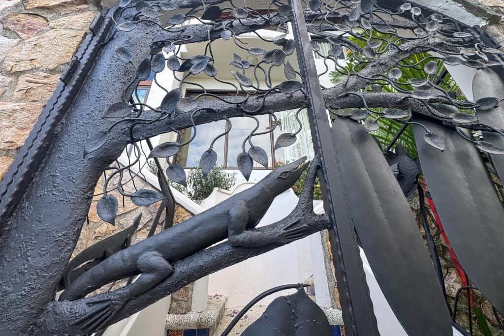 A custom iron gate marks the entrance to the villa, showcasing artistic craftsmanship and nature-inspired details.