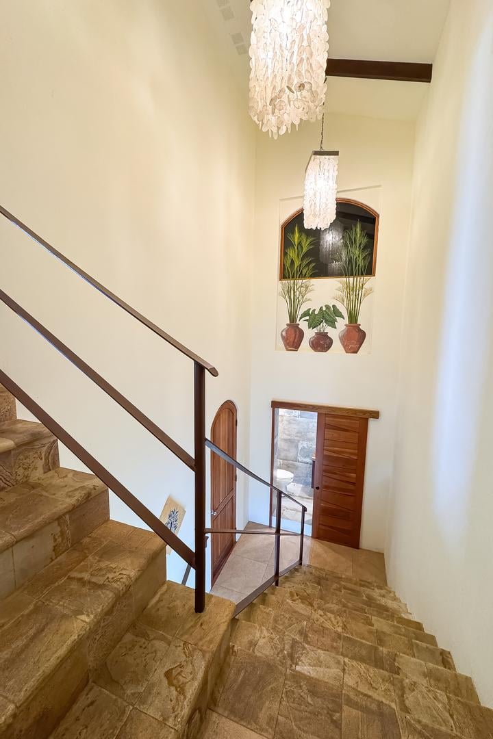 Interior staircase with natural stone steps, metal railing, and hanging light fixtures