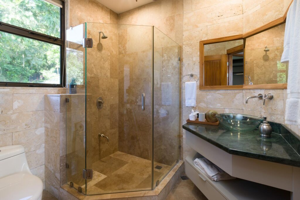 A bright, stone-finished bathroom with a spacious glass shower and modern details, surrounded by the greenery of Manuel Antonio.