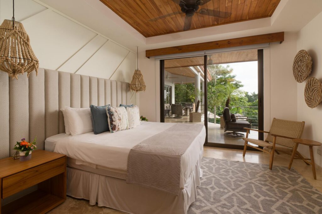A calming bedroom with warm textures, soft neutral tones, and sliding doors that open to a peaceful terrace surrounded by tropical greenery.