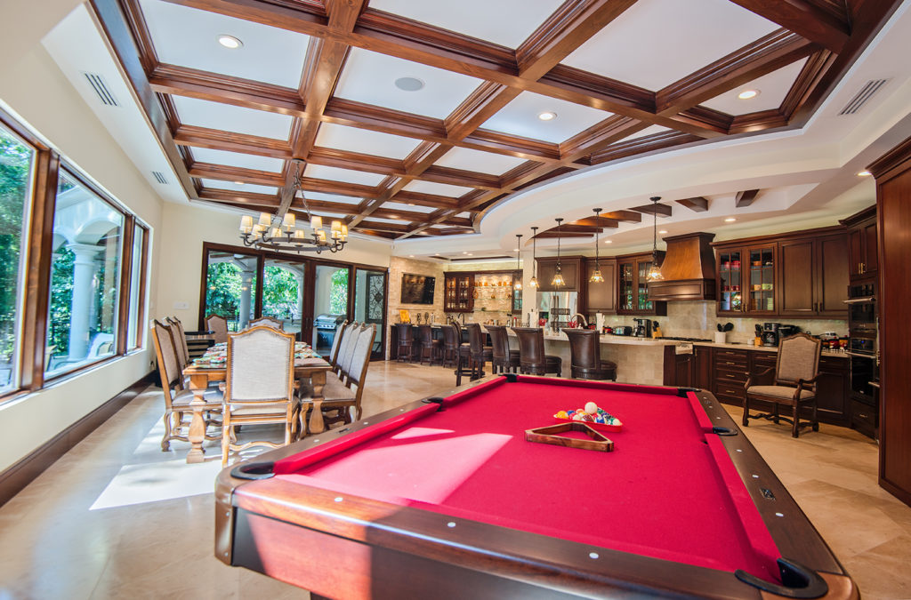Elegance meets entertainment in this open living area, showcasing impeccable interiors and a sleek pool table. Beyond, a view of the pool and vibrant exotic gardens creates a truly enchanting atmosphere.