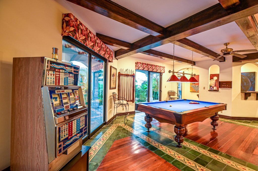 This amazing game room is equipped with a full-sized pool table, a Poker Table, an ornamental slot machine, and a 65-inch SMART HD TV.