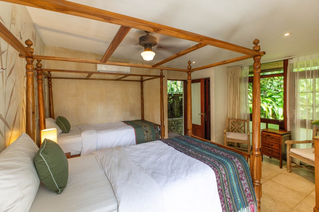 Warm wood, soft textiles, and canopy-style beds define this pool house bedroom, a restful space designed for comfort after days spent between jungle and water.