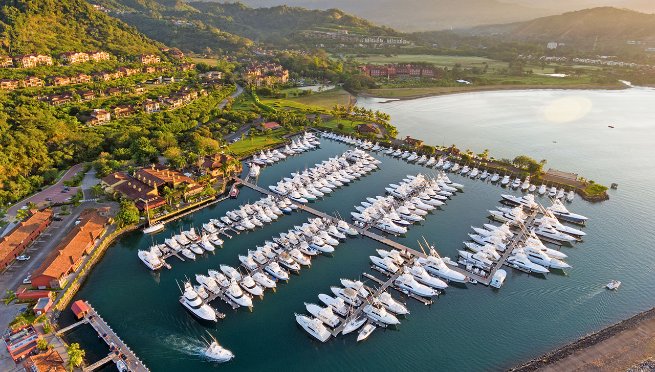 Aerial view of Los Sueños Marina with yachts, boats, and coastline surrounded by tropical hills.