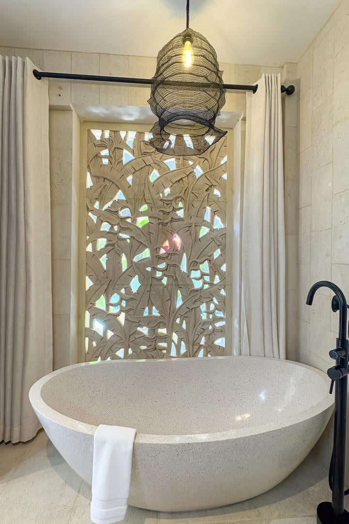 Freestanding stone bathtub set against a carved privacy screen with warm ambient lighting.