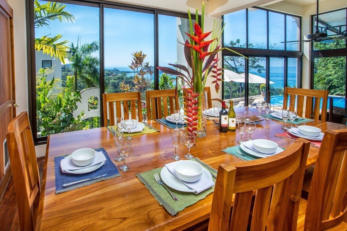 Wooden dining table set for a meal with ocean and jungle views through large glass windows in Manuel Antonio