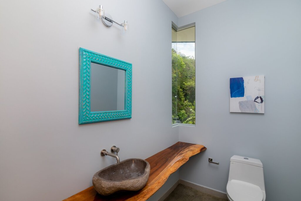 This beautiful bathroom features a stone sink and a clever corner window with a jungle view.