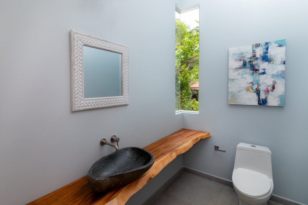 This bathroom features light blue walls, a beautiful sink, and a gorgeous rainforest view.