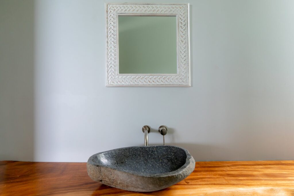 Simple but effective design. A stone bathroom sink sitting on a native wooden counter with a rustic framed mirror above.