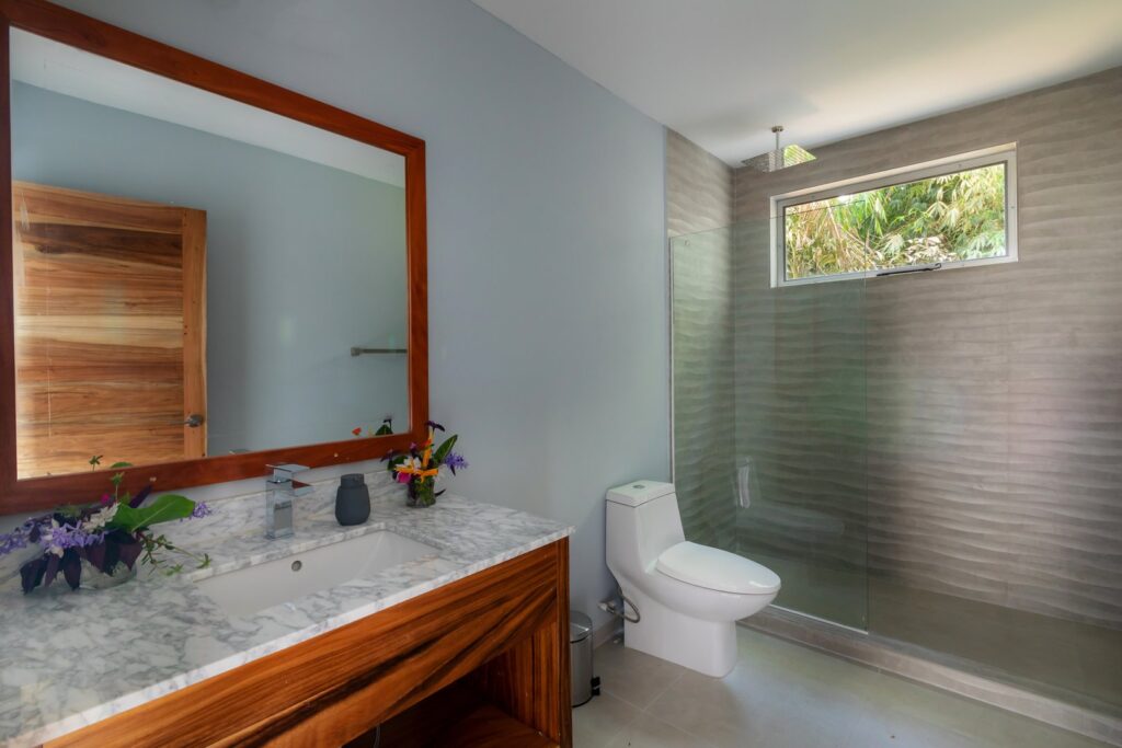 This large bathroom has a sink with native wood details, a large mirror, and a huge luxury shower.
