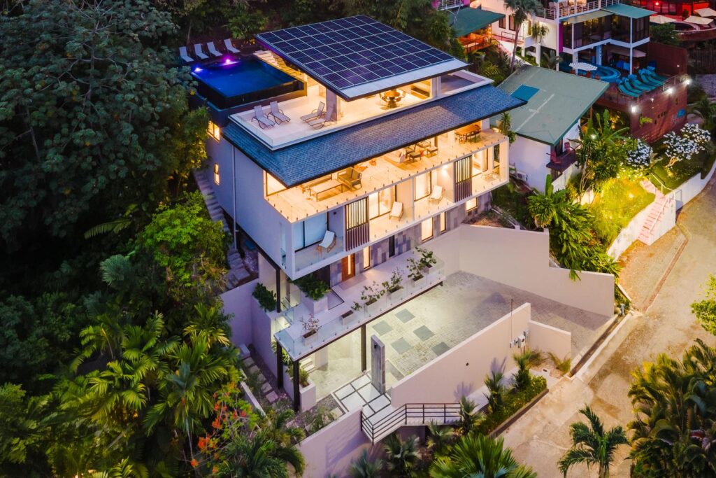 As night falls, the villa comes alive—layered terraces, soft lighting, and the rooftop pool glowing above the jungle.