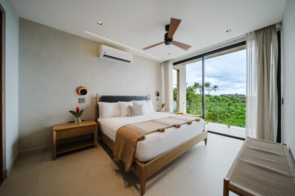 A bright bedroom opening to ocean and lush jungle views and a private terrace.