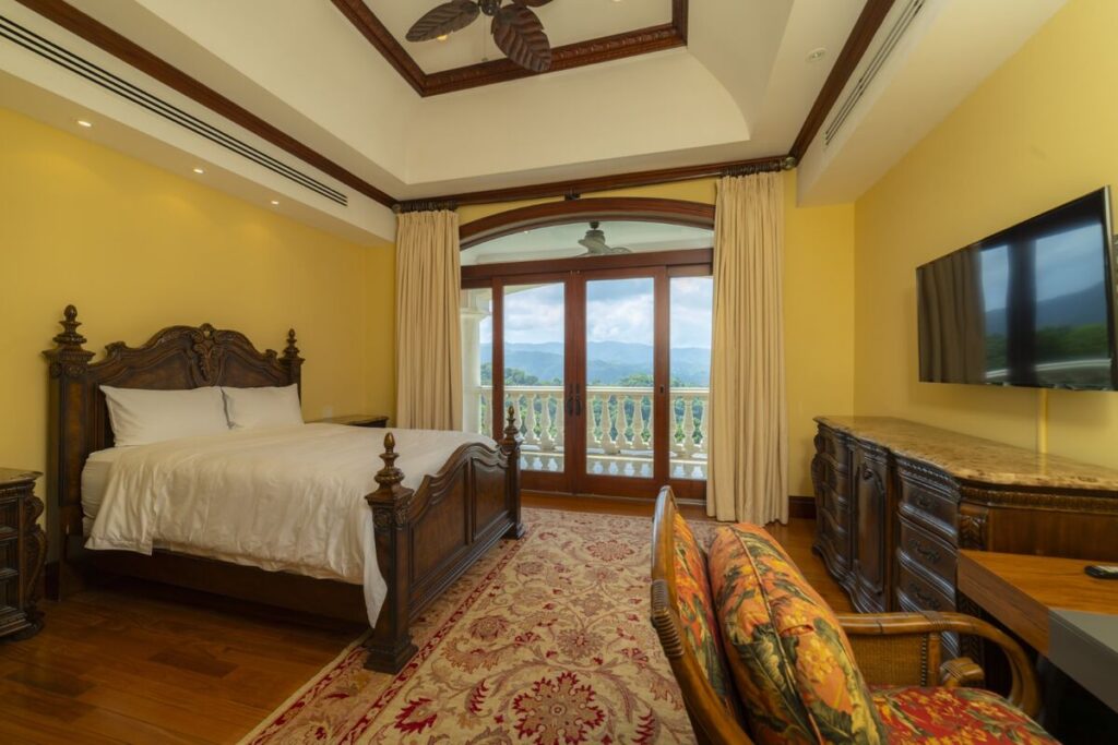 A comfortable bedroom opening to a private balcony, with elevated views across the surrounding hills.