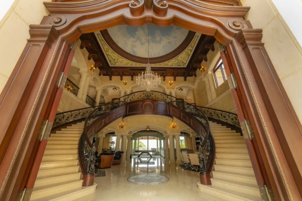 A grand double staircase and soaring ceilings create a dramatic entrance, setting the tone for the home’s refined interiors.