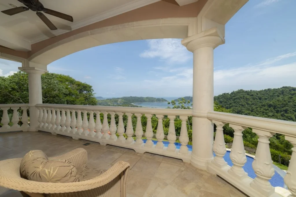 A covered terrace framed by classic columns and arches, overlooking sweeping ocean and jungle views.